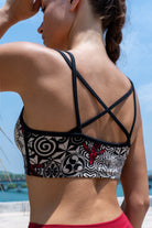 model wearing a cream black nagomi printed cross-back bra from funky simplicity shown from the back with a bridge and a blue river on the background
