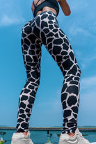 Woman wearing cotton lycra leggings in the cream black cow print shown from the back with a blue sky in the background