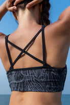 model wearing a greyblack feather cross-back bra from funky simplicity shown from the back with a blue sky and ocean on the background