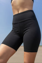 Model wearing black athletic biker shorts  made of cotton stretch against a clear blue sky.