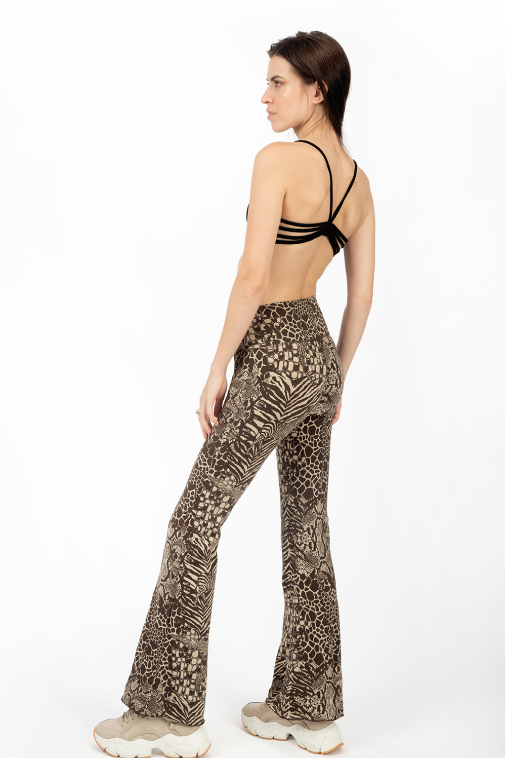 A woman wearing Funky Simplicity wild animal-print flared leggings in cream brown color with black spider bra-top shown from the back 2.