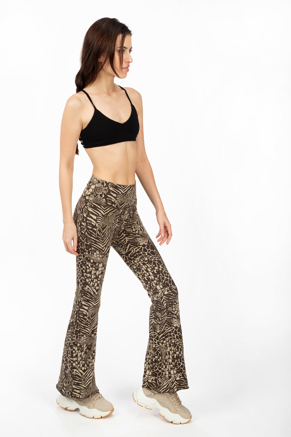 A woman wearing Funky Simplicity wild animal-print flared leggings in cream brown color with black spider bra-top shown from the side.