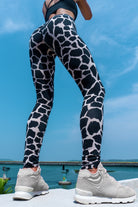 Woman wearing cotton lycra leggings in the cream black cow print shown from the back with a blue sky in the background