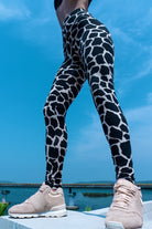 Woman wearing cotton lycra leggings in the cream black cow print shown from the front with a blue sky in the background