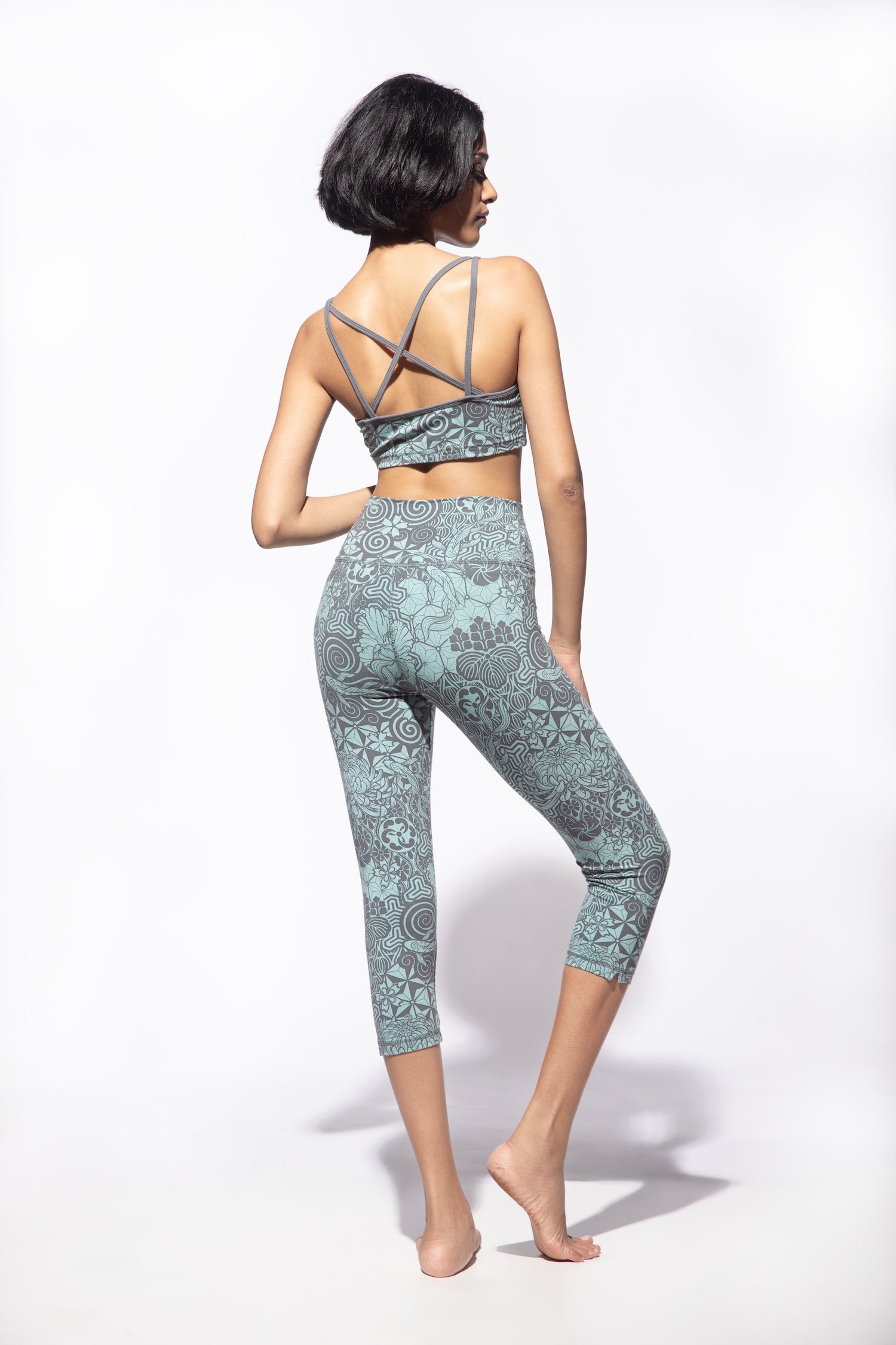 Woman wearing Nagomi Capri leggings in Light Blue (mizu) and light grey. Worn with a matching Cross back bra from Funky Simplicity shown from the back